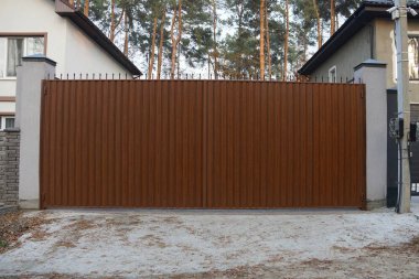 Kırsal bir sokakta büyük kahverengi bir metal kapı ve çit.