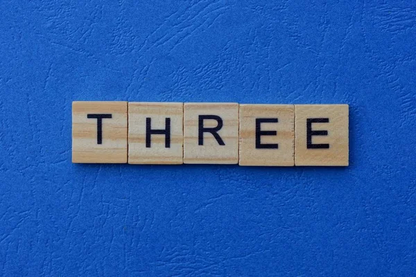 Palabra Tres Hecha Letras Madera Marrón Sobre Fondo Azul —  Fotos de Stock