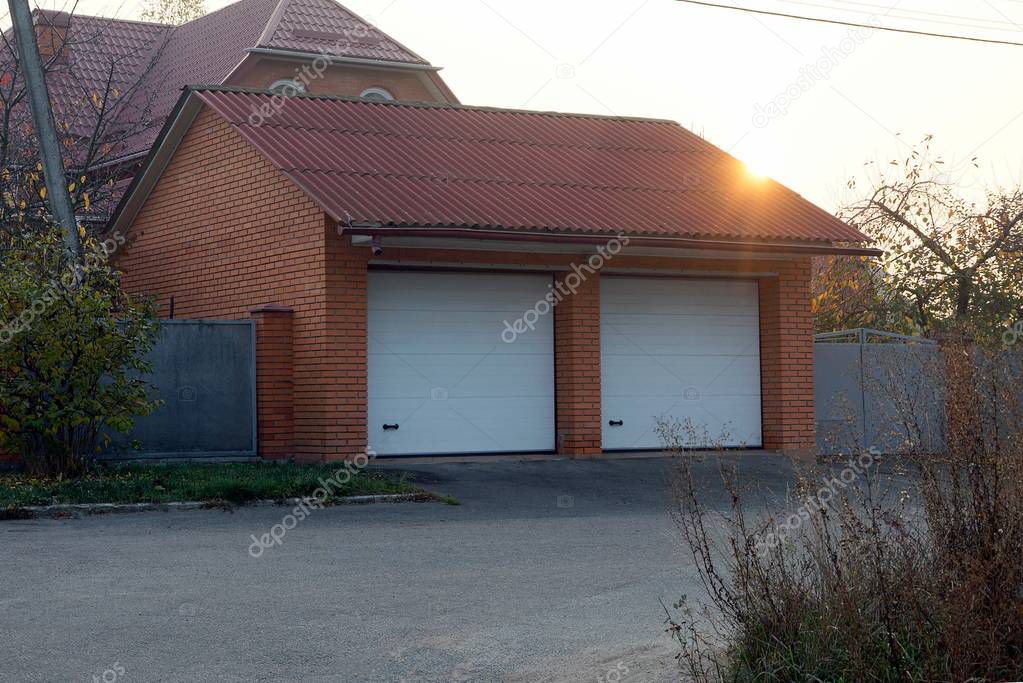 brown brick garage with two white gates on the street by the road