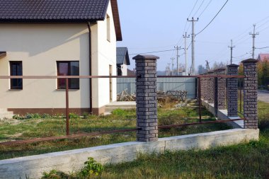 Metal çerçevenin bitmemiş çitleri ve gri beton temelde kahverengi tuğlalar.