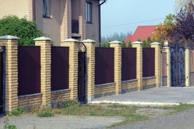 Uzun kahverengi metal çitler, tuğlalar ve yeşil çimenlikteki kapı