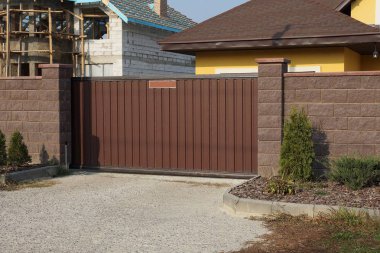 Kırsal bir sokakta büyük kahverengi metal kapı ve tuğla çit