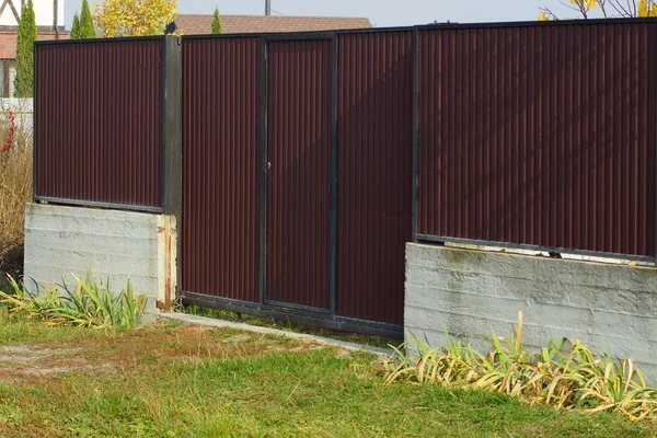 緑の芝生の上の灰色のコンクリート基礎の上の茶色の閉じた門と金属製の柵 — ストック写真