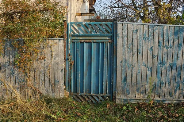 乡村街道上绿色草地上的古老的蓝色金属门和灰色木制栅栏 — 图库照片