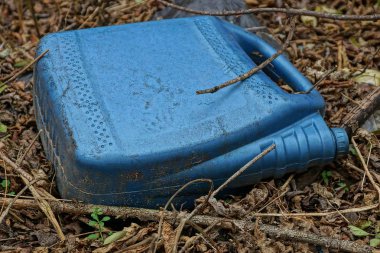 Mavi plastik bir teneke kutunun çöpü kuru çimenlerin üzerinde yatıyor.