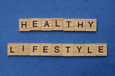 Sağlıklı yaşam biçimi kahverengi ahşap harflerden yapılmıştır. Mavi bir masada yatar.