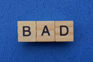 Kahverengi ahşap harflerden yapılmış kötü bir kelime mavi bir masada yatıyor.  