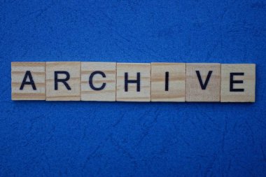 Kahverengi ahşap harflerden yapılmış kelime arşivi mavi bir arkaplanda yatıyor.