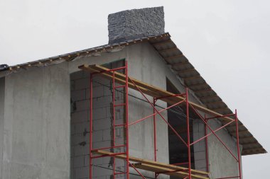 Gökyüzüne karşı tavan arasında boş penceresi olan bitmemiş gri bir evin parçası.