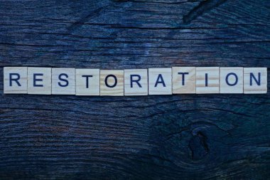 Gri ahşap harflerden yapılan kelime restorasyonu gri bir masada yatıyor.