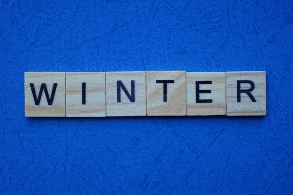 茶色の木の文字で作られた単語の冬は青い背景にあります — ストック写真