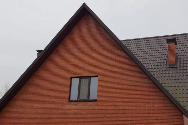 屋根裏部屋のある茶色のレンガ造りの家のファサードと灰色の空に対する1つの窓 — ストック写真