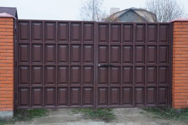 Büyük kapalı demir kahverengi kapı ve sokaktaki tuğla çitin bir kısmı
