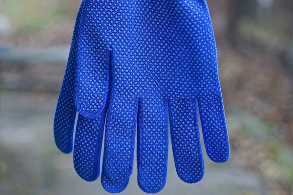 two blue work gloves hanging against a gray background