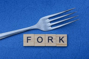 Bir metal çatal ve ahşap harflerden gelen sözcük mavi bir masada yatıyor.