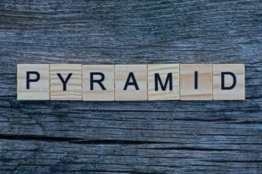  Kelime piramidi gri ahşap harflerden yapılmıştır. Gri bir masada yatar.