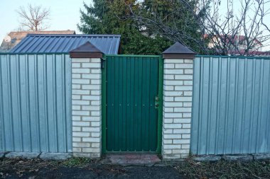 Kırsal bir sokakta yeşil demir kapı ve gri metal ve tuğla çit