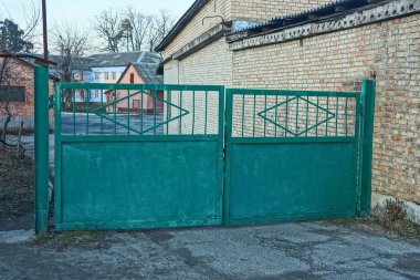 Kırsal bir sokakta büyük yeşil demir bir kapı.