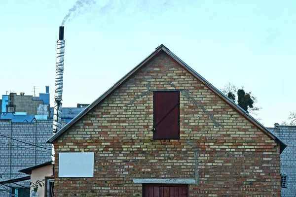 茶色のレンガ造りの家の屋根裏部屋木製のドアと青い空に対する煙突 — ストック写真
