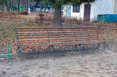 Bir sonbahar parkında bir ara sokakta duran kahverengi ahşap bir bank.