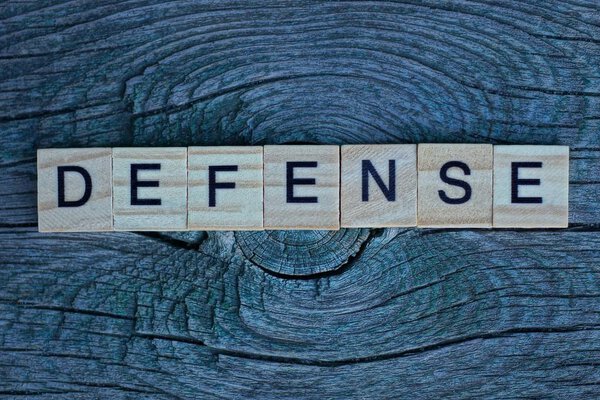 word defence from small letters lies on a gray wooden board