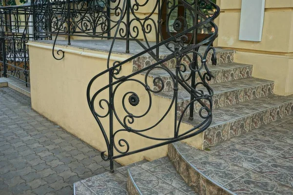 black iron bar handrails in a forged pattern and brown concrete steps on the street