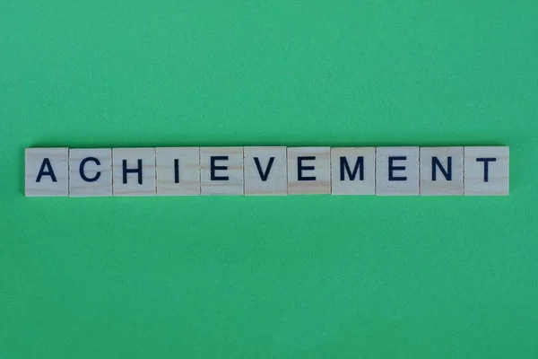 word achievement made of small gray wooden letters on a green paper background