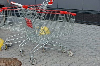 İki boş gri metal tramvay. Tekerlekli kırmızı saplı. Kaldırımda duvarın karşısında duruyor.