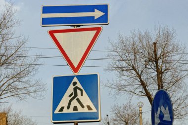 Sokakta gökyüzüne karşı demir bir sütunda üç yol işareti.