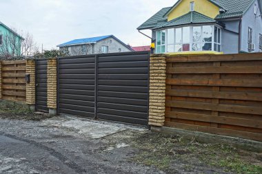 Büyük, kahverengi demir bir kapı ve kırsal bir sokakta tahta ve tuğlalardan oluşan bir çitin parçası.