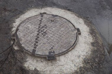 Gri betonda bir demir kahverengi lağım deliği ıslak zeminde ve dışarıda da su.