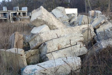Eski gri beton bloklar ve levhalar dışarıdaki kuru ot ve bitki örtüsünde yatıyor.