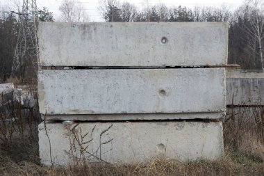 Eski gri beton bloklar ve beton levhalar dışarıdaki kuru çimenlerde yatıyor.