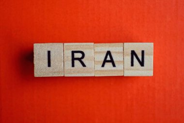 İran kelimesi kırmızı kağıtta küçük gri ahşap harflerden oluşur.