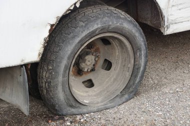 Gri asfaltta beyaz bir arabanın siyah lastiği patladı.