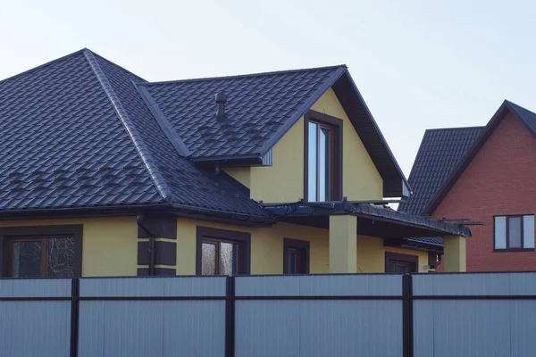 灰色の金属製のフェンスの後ろに茶色のタイル張りの屋根の下に緑の壁と窓のある大きな民家の一部 — ストック写真