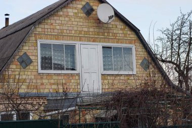 Kahverengi tuğlalı bir evin tavan arası. İki beyaz penceresi ve gökyüzüne bakan bir kapısı var.