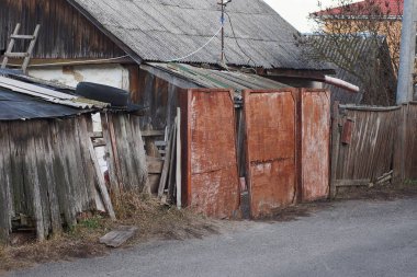 Paslı kırmızı demir kapı ve kırsal bir sokakta tahta tahtaların kırık gri çiti.