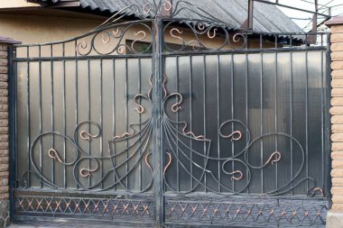 İşlenmiş demir çubuklardan bir siyah demir kapı ve sokaktaki kahverengi tuğlalardan bir parça.