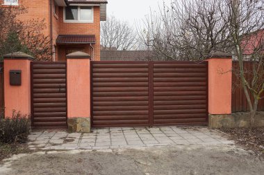 Büyük kahverengi kapı ve ahşap tahtalardan yapılmış çitin bir kısmı ve kırsal bir sokakta beton.