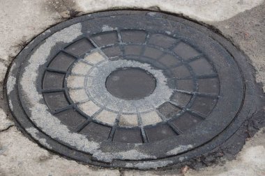 Eski ve ıslak bir demir kanalizasyon kanalı sokaktaki gri asfaltta yatıyor.