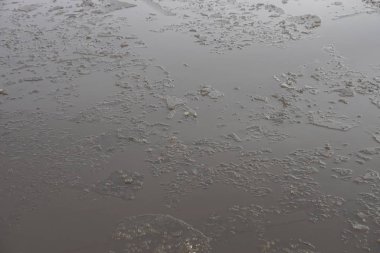 Gri buz parçalarının deseni... Kahverengi kirli sularda... Sokakta büyük bir su birikintisi...