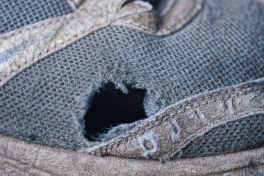 Eski bir spor ayakkabısının gri kumaşında büyük bir kara delik.