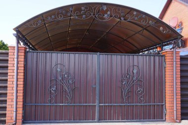 Güneşli bir günde, büyük kahverengi metal kapılı ve tuğladan bir çitin parçası.