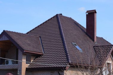 Güneşli bir günde mavi gökyüzüne karşı penceresi ve tuğladan bacası olan kahverengi kiremitli bir çatı altında özel bir evin parçası.