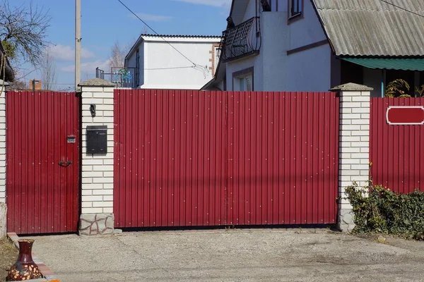 阳光灿烂的乡村街道上的大红铁门和白砖墙 — 图库照片