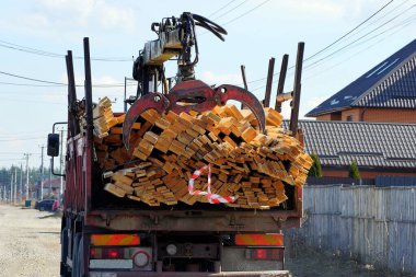 Kahverengi tahtalarla dolu demir vinçli büyük bir kamyon yolda ilerliyor.