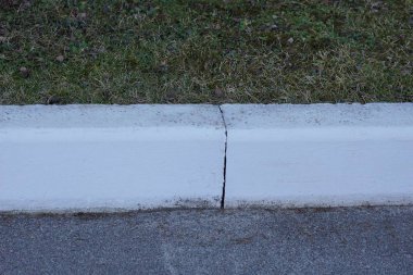 Gri asfalt yolda ve çimlerde beyaz beton bir kaldırım.