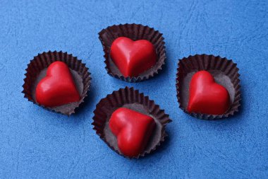 dört kırmızı kalp şekeri kahverengi kağıt paketlerde mavi bir masada.