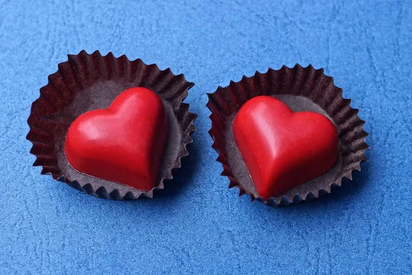 two red heart candies in brown paper packages on a blue table